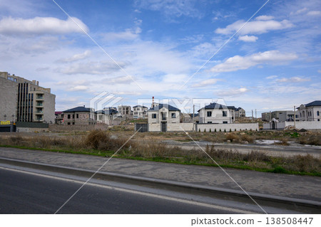 Suburban neighborhood with modern houses along paved road under bright sky Suburban neighborhood with modern houses along paved road under bright sky 138508447
