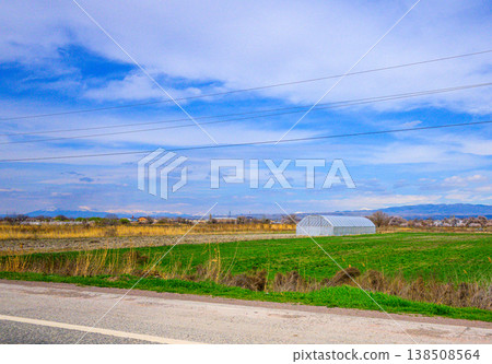 Peaceful countryside view with fields, road, and power lines under sunny sky Peaceful countryside view with fields, road, and power lines under sunny sky 138508564