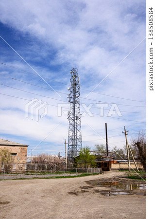 Utility tower in rural area under partly cloudy sky with dirt road and puddles Utility tower in rural area under partly cloudy sky with dirt road and puddles 138508584