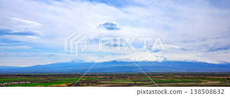 Panoramic view of rolling hills and snow-dusted peaks under a soft blue sky Panoramic view of rolling hills and snow-dusted peaks under a soft blue sky 138508632