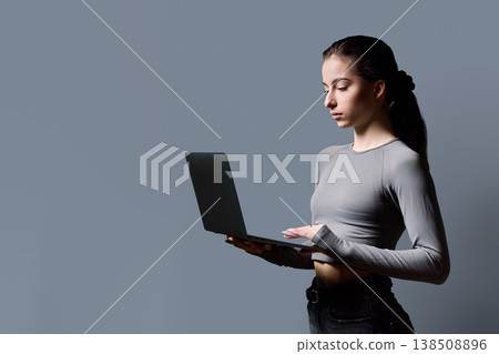 Profile portrait of serious teenage girl using laptop on gray background 138508896