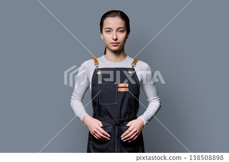Portrait of young serious female student in apron on gray background Portrait of young serious female student in apron on gray background 138508898