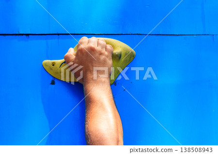 Male climber hand gripping hold on the blue climbing wall 138508943