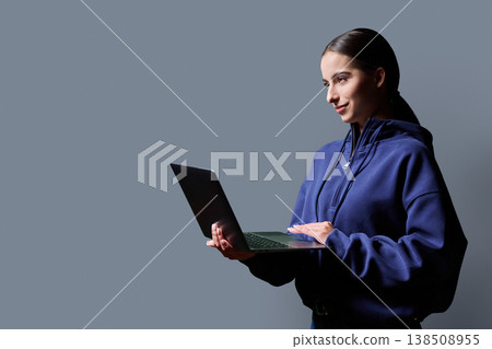 Portrait of smiling teenage girl holding laptop on gray studio background Portrait of smiling teenage girl holding laptop on gray studio background 138508955