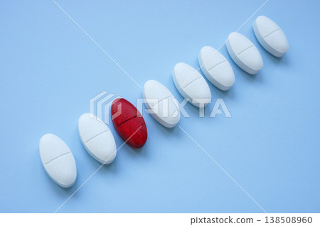 Red pill among white tablets depicting uniqueness. 138508960