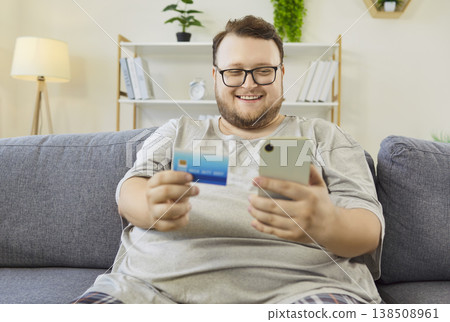Plus-size man confirms online payment with credit card and smartphone on the couch 138508961