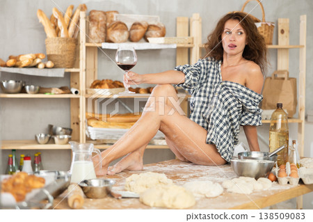 Woman in shirt sitting on table with wine in bakery Woman in shirt sitting on table with wine in bakery 138509083