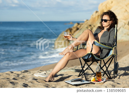 Naked woman in unbuttoned blazer sitting by ocean with whiskey Naked woman in unbuttoned blazer sitting by ocean with whiskey 138509085