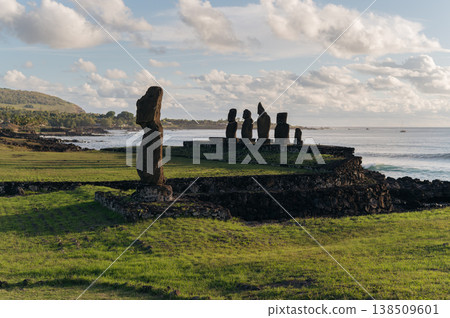 Majestic moai stone statue stands on green grassy coast of rapa nui easter island under bright cloudy sky offering serene mysterious expression overlooking vast blue ocean Majestic moai stone statue stands on green grassy coast of rapa nui easter island under bright cloudy sky offering serene mysterious expression overlooking vast blue ocean 138509601