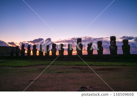 Majestic moai statue silhouette stands against vibrant sunset sky on easter island rapa nui evoking peaceful mysterious ancient history across wide rugged green grassy landscape Majestic moai statue silhouette stands against vibrant sunset sky on easter island rapa nui evoking peaceful mysterious ancient history across wide rugged green grassy landscape 138509608