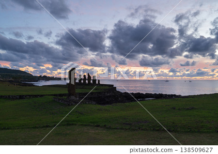 Majestic moai statue silhouette stands quietly on green easter island coast during peaceful sunset over ocean. serene rapa nui landscape features heavy dark cloud filling sky Majestic moai statue silhouette stands quietly on green easter island coast during peaceful sunset over ocean. serene rapa nui landscape features heavy dark cloud filling sky 138509627