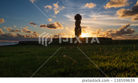 Majestic moai statue silhouette stands peacefully on easter island under breathtaking sunset sky representing mysterious ancient rapa nui culture with bright golden sun ray over green grass field Majestic moai statue silhouette stands peacefully on easter island under breathtaking sunset sky representing mysterious ancient rapa nui culture with bright golden sun ray over green grass field 138509639