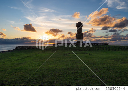 Majestic moai statue stands peaceful on vibrant green grass during dramatic sunset over ocean on rapa nui easter island projecting mysterious ancient presence against cloudy sky Majestic moai statue stands peaceful on vibrant green grass during dramatic sunset over ocean on rapa nui easter island projecting mysterious ancient presence against cloudy sky 138509644