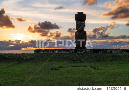 Majestic ancient moai statue stands solemn and proud on green grass of easter island rapa nui overlooking calm ocean under dramatic vibrant sunset sky filled with warm light Majestic ancient moai statue stands solemn and proud on green grass of easter island rapa nui overlooking calm ocean under dramatic vibrant sunset sky filled with warm light 138509646