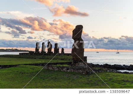 Majestic moai stone statue stands on peaceful grassy coast of easter island overlooking ocean at sunset while ancient rapa nui monolith group rests in awe under colorful cloud 138509647