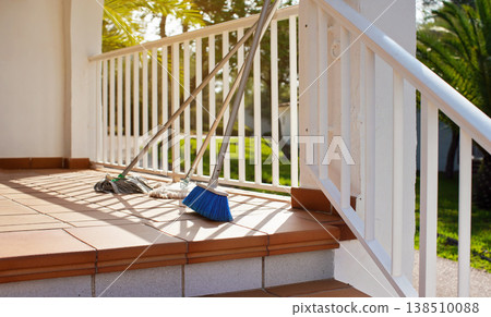 Brooms and mops leaning on white fence at hotel room terrace, morning sun shines on, blurred palm trees background - cleaning in tourist resort concept Brooms and mops leaning on white fence at hotel room terrace, morning sun shines on, blurred palm trees background - cleaning in tourist resort concept 138510088
