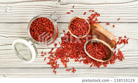Dried goji aka. wolfberry seeds inside glass bottle, some in wooden bowls and spilled on white boards desk, view from above Dried goji aka. wolfberry seeds inside glass bottle, some in wooden bowls and spilled on white boards desk, view from above 138510129