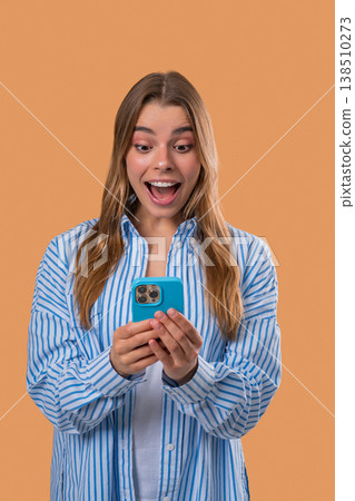 Shocked woman with smartphone on beige studio with open mouth. Amazed lady, app 138510273