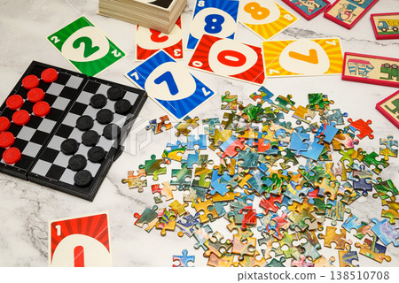 puzzle pieces, cards and checkers board in disarray on a marble table puzzle pieces, cards and checkers board in disarray on a marble table 138510708