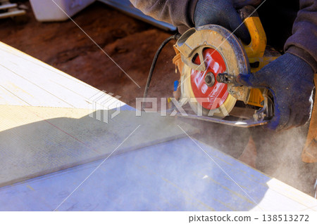 Carpenter operates circular hand saw to cut through wood on construction site dust, debris fly. Carpenter operates circular hand saw to cut through wood on construction site dust, debris fly. 138513272