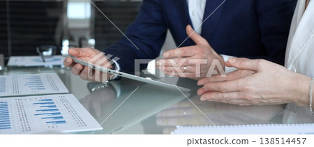 Business partners collaborating on financial data, discussing market trends, analyzing charts, and reviewing reports on a tablet during an office meeting. Concept of teamwork, finance, and 138514457