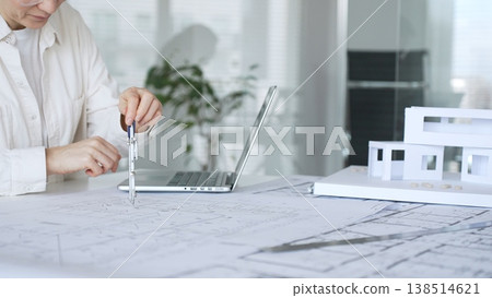 Woman architect working at an office desk, analyzing blueprints, using a laptop, and preparing a modern house model, representing innovative construction and design processes Woman architect working at an office desk, analyzing blueprints, using a laptop, and preparing a modern house model, representing innovative construction and design processes 138514621