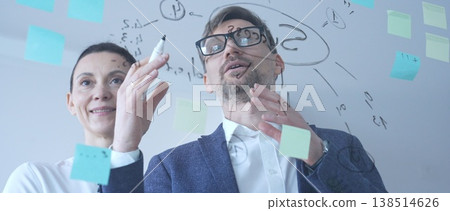 Businessman intently creating a detailed mind map and arranging sticky notes on a transparent board, developing innovative ideas for strategic planning and problem solving 138514626