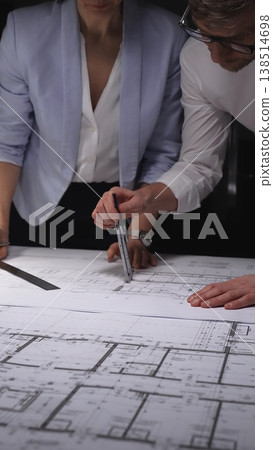 Architects and engineers collaborating on a building blueprint, measuring and discussing plans for a new construction project. Concept of architecture and business in low key lighting 138514698