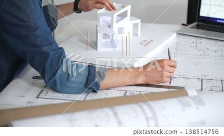Architect hands reviewing building blueprints and housing plans on a table, utilizing a laptop for architectural drawing and design while planning a construction project Architect hands reviewing building blueprints and housing plans on a table, utilizing a laptop for architectural drawing and design while planning a construction project 138514756