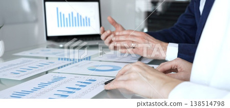 Group of business professionals working together in a modern office, reviewing financial reports, charts, and laptop data on a glass meeting table. Concept of teamwork, collaboration, and success 138514798
