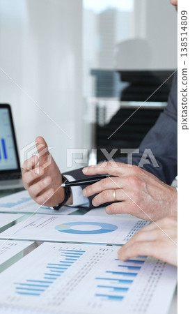 Businessman's hands analyzing financial data and charts on documents during a meeting, focusing on strategic planning and corporate growth in an office setting Businessman's hands analyzing financial data and charts on documents during a meeting, focusing on strategic planning and corporate growth in an office setting 138514809