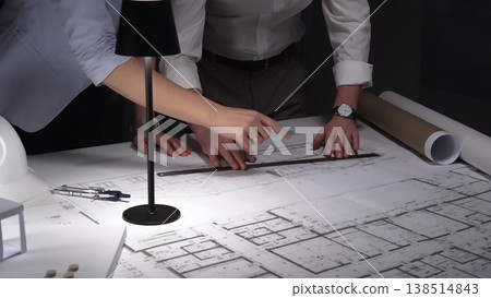 Collaborative team working on an engineering project, reviewing floor plans with a lamp illuminating the architectural drawings. Business and architect people concept Collaborative team working on an engineering project, reviewing floor plans with a lamp illuminating the architectural drawings. Business and architect people concept 138514843