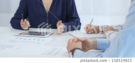 Professional colleagues examining financial documents, studying performance charts on paper and digital tablet during collaborative meeting in modern workplace setting 138514923