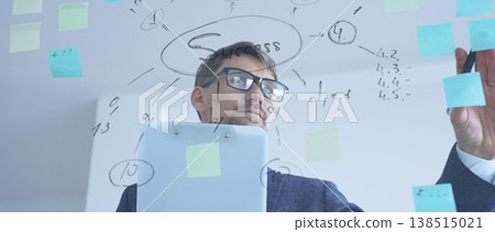 Experienced business professional developing a strategic success plan, writing on a transparent whiteboard with sticky notes while working on a long term company vision 138515021