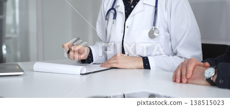 Experienced female doctor providing medical guidance to a male patient and filling out a prescription form during a hospital visit. Medicine, healthcare and science concept Experienced female doctor providing medical guidance to a male patient and filling out a prescription form during a hospital visit. Medicine, healthcare and science concept 138515023