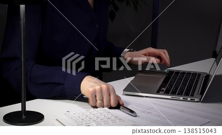 Woman working late on laptop, hands typing on keyboard, managing business paperwork at desk in office at night. Audit and taxes in business Woman working late on laptop, hands typing on keyboard, managing business paperwork at desk in office at night. Audit and taxes in business 138515043