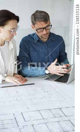Architects collaborating on blueprint plans, discussing engineering details and project designs, planning construction development with a laptop in a modern office environment Architects collaborating on blueprint plans, discussing engineering details and project designs, planning construction development with a laptop in a modern office environment 138515116