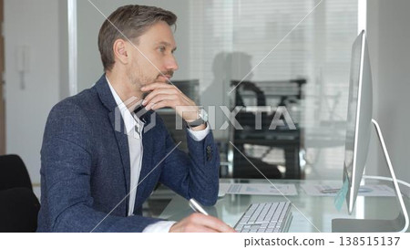 Businessman in a blue jacket thinking and brainstorming ideas while working on computer and taking notes in modern office. Business people concept Businessman in a blue jacket thinking and brainstorming ideas while working on computer and taking notes in modern office. Business people concept 138515137