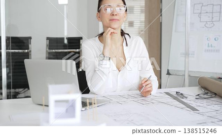 Professional architect woman working on architectural plans. Finding inspiration for a new building project. Smiling with satisfaction and confidence in her modern office 138515246