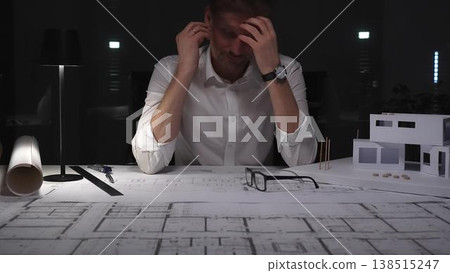Architect experiencing burnout and stress, working late at night in a dark office with building models and blueprints. Architect experiencing burnout and stress, working late at night in a dark office with building models and blueprints. 138515247
