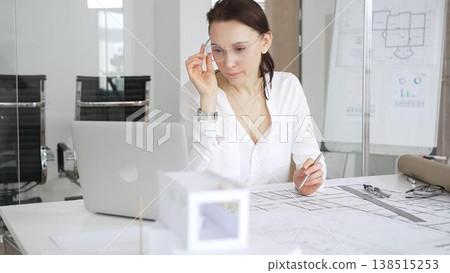 Female architect designing new blueprints for a project, reflecting on building plans and architectural models in a modern office environment, thinking about construction and innovation Female architect designing new blueprints for a project, reflecting on building plans and architectural models in a modern office environment, thinking about construction and innovation 138515253