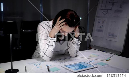 Businesswoman clutching her head in a dim office, surrounded by paperwork and a tablet while working late, showing exhaustion, headache and overwhelming professional stress Businesswoman clutching her head in a dim office, surrounded by paperwork and a tablet while working late, showing exhaustion, headache and overwhelming professional stress 138515254