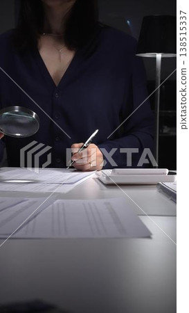 Woman examining tax forms and financial statements at desk, using calculator and magnifying glass to verify figures and audit records. Audit and taxes theme in business 138515337