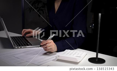 Woman's hands typing on laptop at office desk, working late night with calculator and financial documents. Audit and taxes in business 138515343