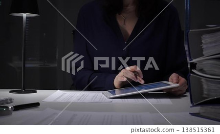 Woman working late night in office, multitasking with a tablet and writing on documents, managing heavy paperwork load. Audit and taxes in business Woman working late night in office, multitasking with a tablet and writing on documents, managing heavy paperwork load. Audit and taxes in business 138515361