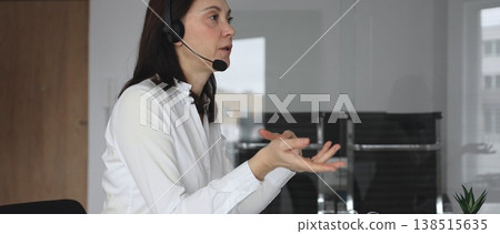 Businesswoman in a white shirt and headset leading a video call from a modern office, presenting with a tablet and gesturing as she discusses strategy and trains remote colleagues Businesswoman in a white shirt and headset leading a video call from a modern office, presenting with a tablet and gesturing as she discusses strategy and trains remote colleagues 138515635