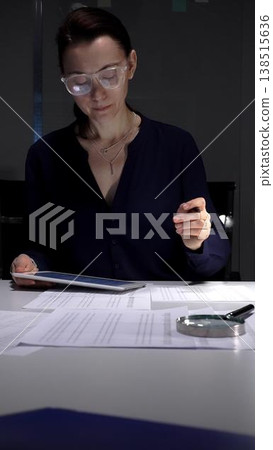 Woman working late, signing documents and analyzing data on a tablet by office lamp light at night. Audit and taxes in business 138515636