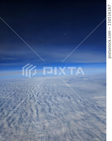 Stunning high-altitude view of a vast, textured sea of clouds beneath a clear blue atmosphere, taken from an airplane window. 138516167
