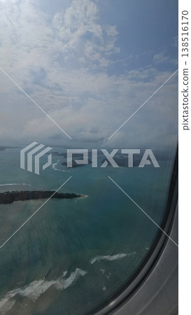 Vertical airplane window view capturing the edge of the aircraft overlooking scattered tropical islands in the Andaman Sea under cloudy skies. 138516170