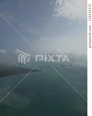 Moody, atmospheric aerial view of lush, dark green Andaman islands emerging from the ocean surrounded by low-hanging mist and clouds. 138516171